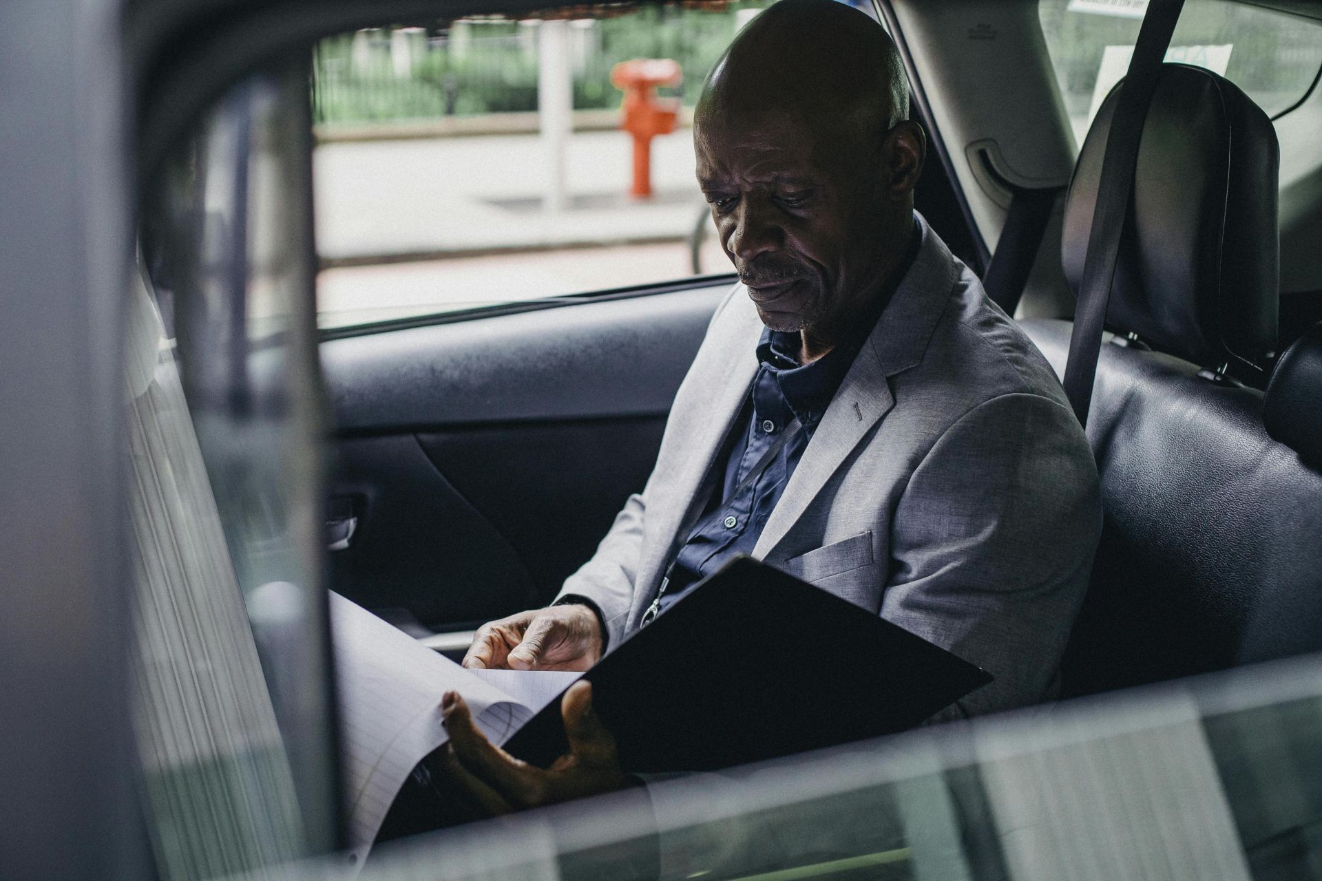 Side view serious African American businessman in formal clothes sitting in car back seat and reading documents